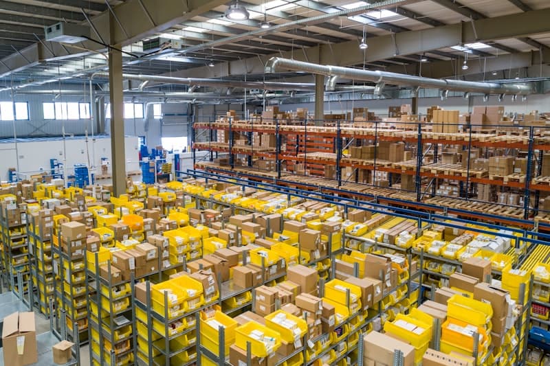 Warehouse interior with exposed steel roof framing, storage racks, and material handling conveyors